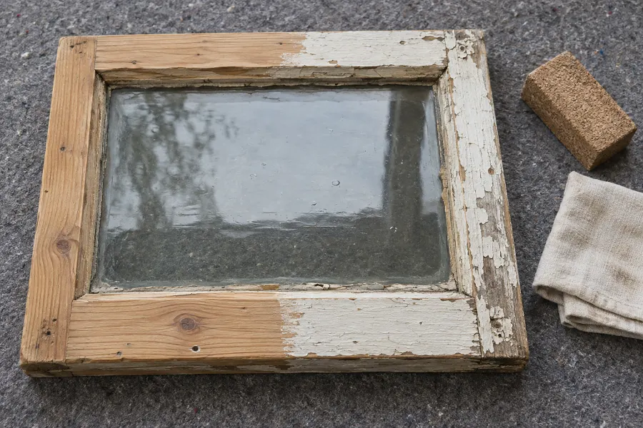 Alter Fensterflügel, zur Hälfte bis aufs Holz abgeschliffen, daneben ein Schleifklotz